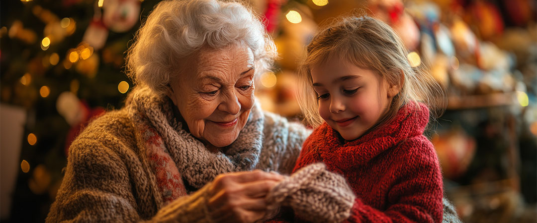 An elderly woman with her granddaughter sat in front of a christmas tree smiling.